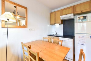 A compact kitchen with wooden cabinets, a white refrigerator, a microwave, and a wooden dining table with chairs. - Apartment in Orcières by Ski Slopes & Pool (Orcières)