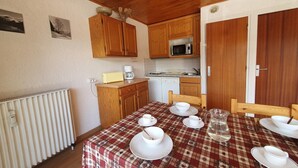 A compact kitchen with wooden cabinets, a microwave, and a dining area with a checkered tablecloth. - Alpine Apartment for 8 guests (Les Deux Alpes)