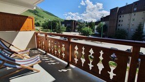 A balcony with a wooden railing, a view of a street, and a mountain in the background. - Alpine Apartment for 8 guests (Les Deux Alpes)