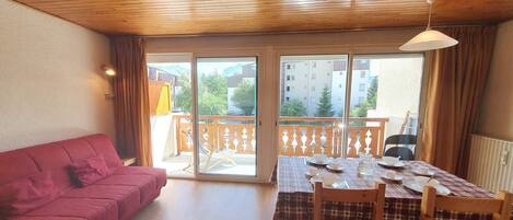 A room with a red sofa, a dining table set with plates, and a view of a balcony with a railing.