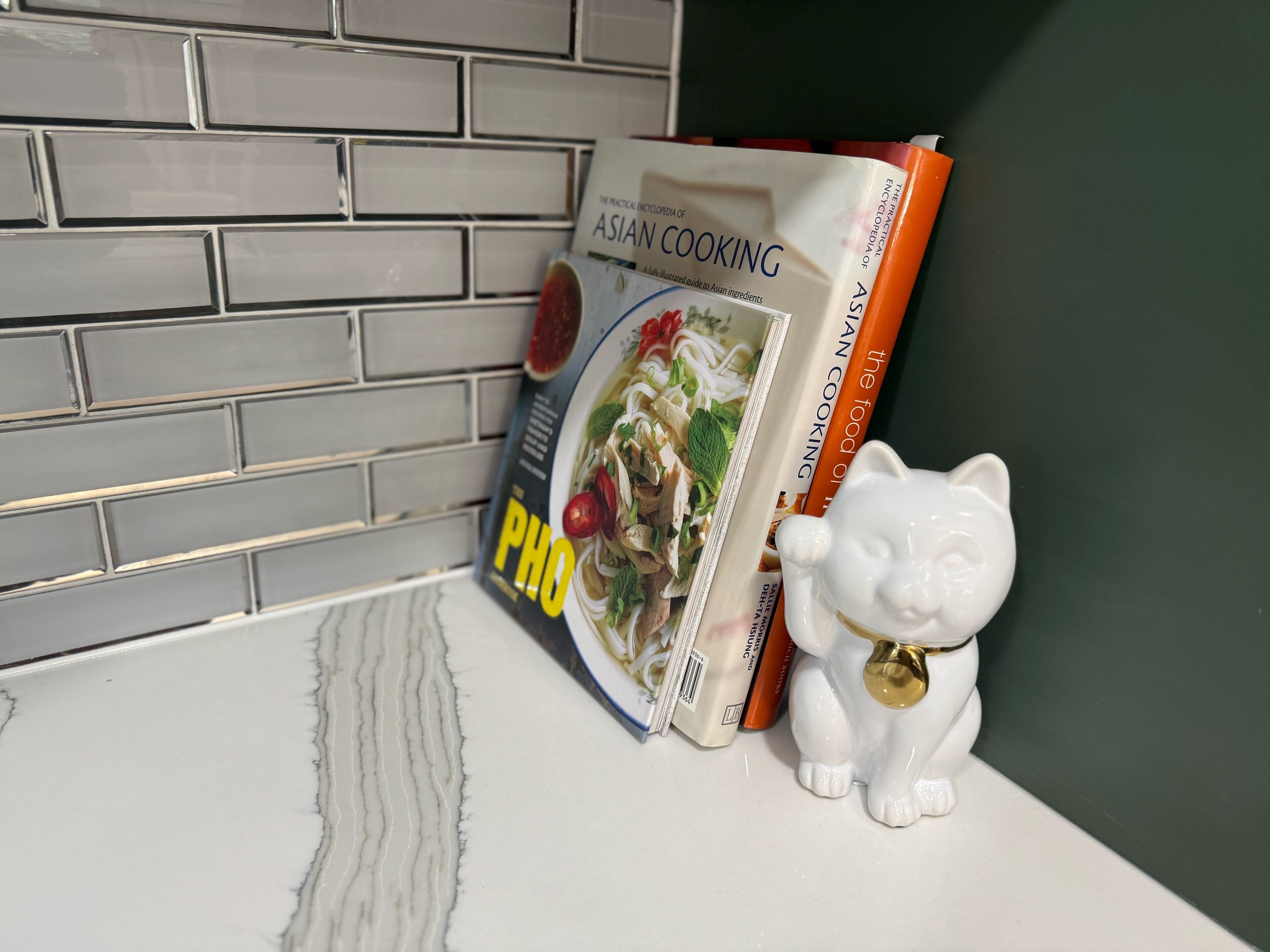 Un comptoir de cuisine orné d’une figurine d’éléphant en céramique blanche, d’un livre de cuisine intitulé « L’encyclopédie pratique de la cuisine asiatique » et d’un paquet de nouilles pour le plat pho.