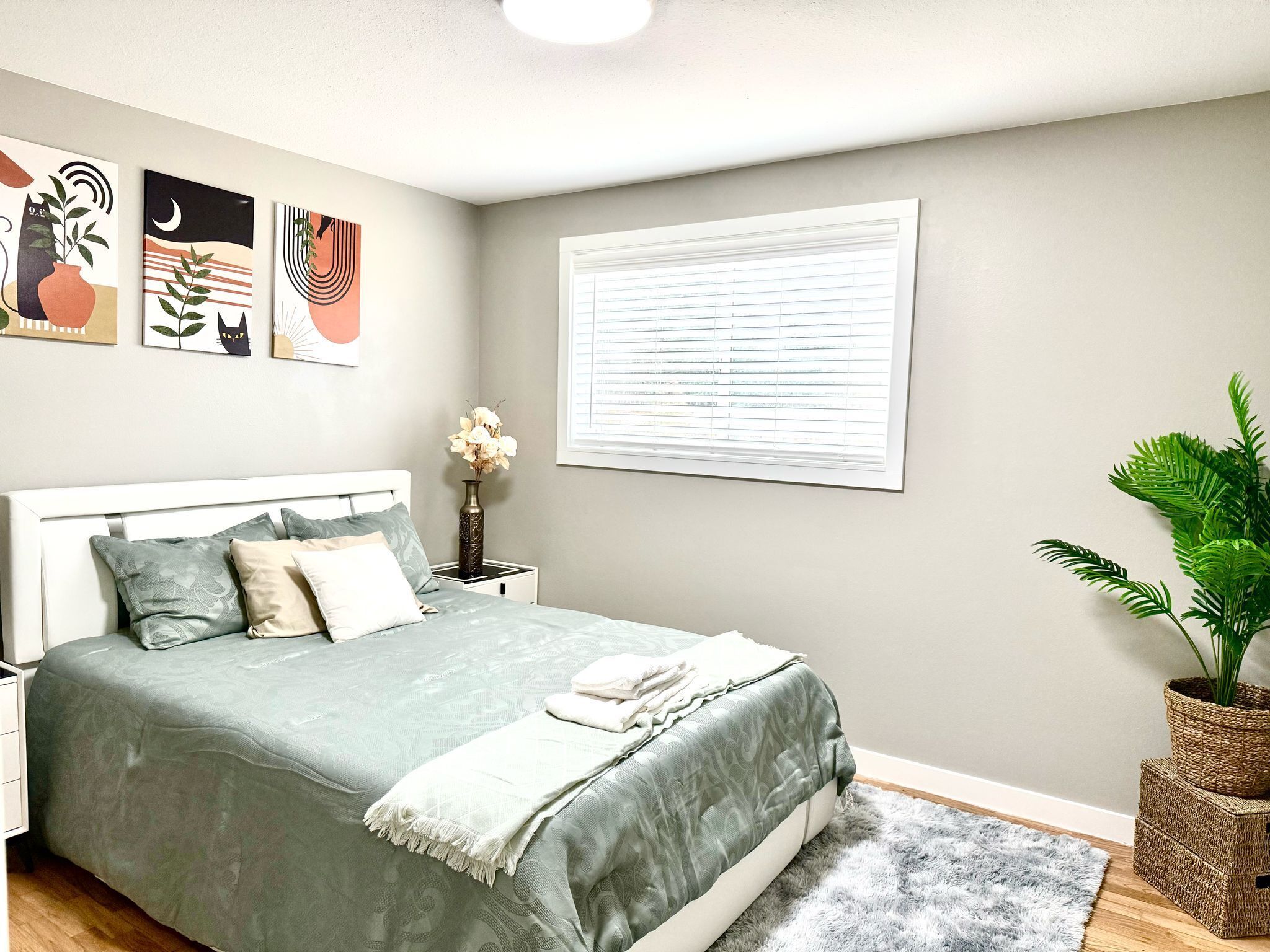 A bedroom with a bed, a nightstand, a window with blinds, and wall art.