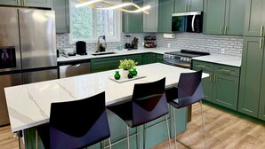 Una cocina moderna con gabinetes verdes, una isla de mármol blanco y taburetes negros.