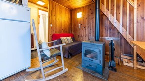 Un accogliente interno di una baita con arredamento in legno, un letto, una poltrona a dondolo, un fornello e un frigorifero bianco.