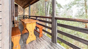 Un terrazzo in legno con tavolo e panche, circondato da una ringhiera di legno, con vista su una zona boschiva.