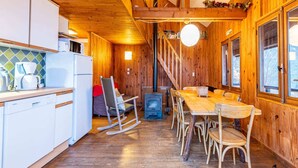 Interno di una baita in legno con cucina, zona pranzo e camino.