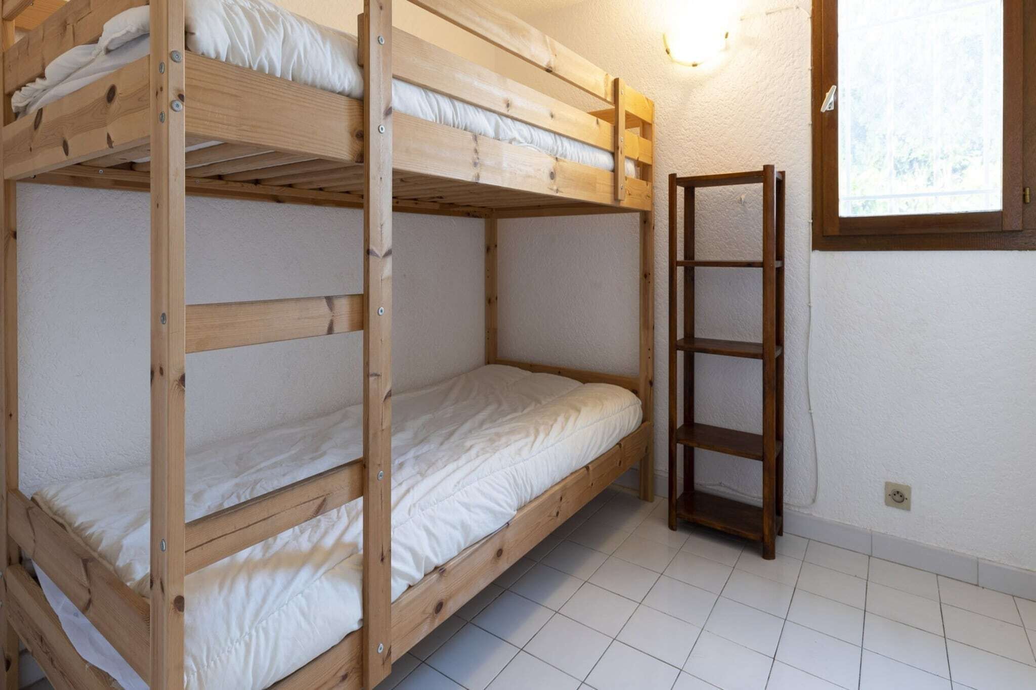 A bunk bed room with a wooden ladder, white bedding, and a window with a view.
