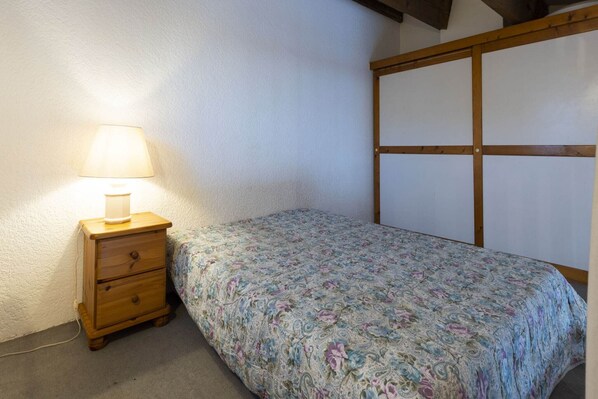 A small bedroom with a single bed, a nightstand with a lamp, and a wooden headboard.
