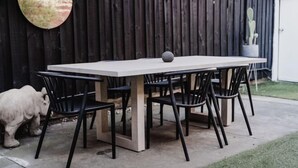 A rectangular outdoor table with six chairs, a stone sphere on the table, and a cactus in a pot to the right.
