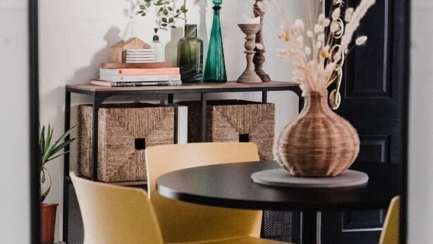 A dining area with a round table, yellow chairs, a small console table with decorative items, and a potted plant.