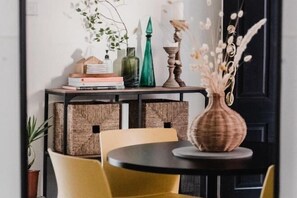 Un comedor con una mesa redonda, sillas amarillas, una pequeña consola decorada con objetos y una planta en maceta.