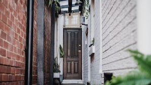 A narrow alleyway with a wooden door at the end, flanked by brick walls and potted plants.