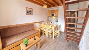 Una habitación acogedora con un sofá de madera, una mesa de comedor con sillas, una pequeña cocina y una escalera de madera.