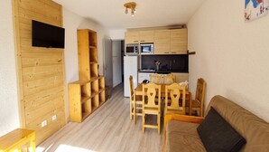 Ein kompakter Wohnraum mit Küchenzeile, Holzmöbeln, einem Flachbildfernseher und einer Essecke.