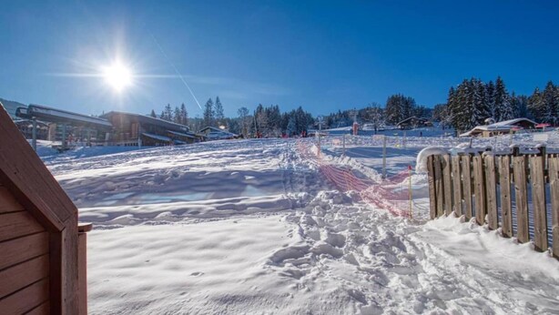 Schneebedeckte Landschaft mit einem Holzbauten und einer Seilbahn im Hintergrund.