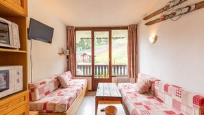 A cozy room with two wooden sofas, a wooden table, a television, and a sliding glass door leading to an outdoor area. - Apartment in Morillon near Ski Resort (Morillon)