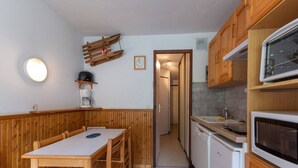 A compact kitchen with wooden cabinets, a microwave, a coffee maker, and a dining area with a table and chairs. - Apartment in Morillon near Ski Resort (Morillon)