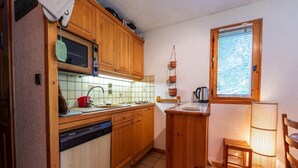 Cozinha compacta com armários de madeira, micro-ondas, pia e janela com persianas.