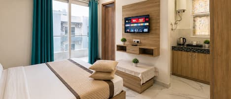 Ein Hotelzimmer mit einem Bett, einem an einer Holzvertäfelung montierten Fernseher, einem kleinen Tisch mit einer Pflanze und einem Badezimmer mit Toilette und Waschbecken.