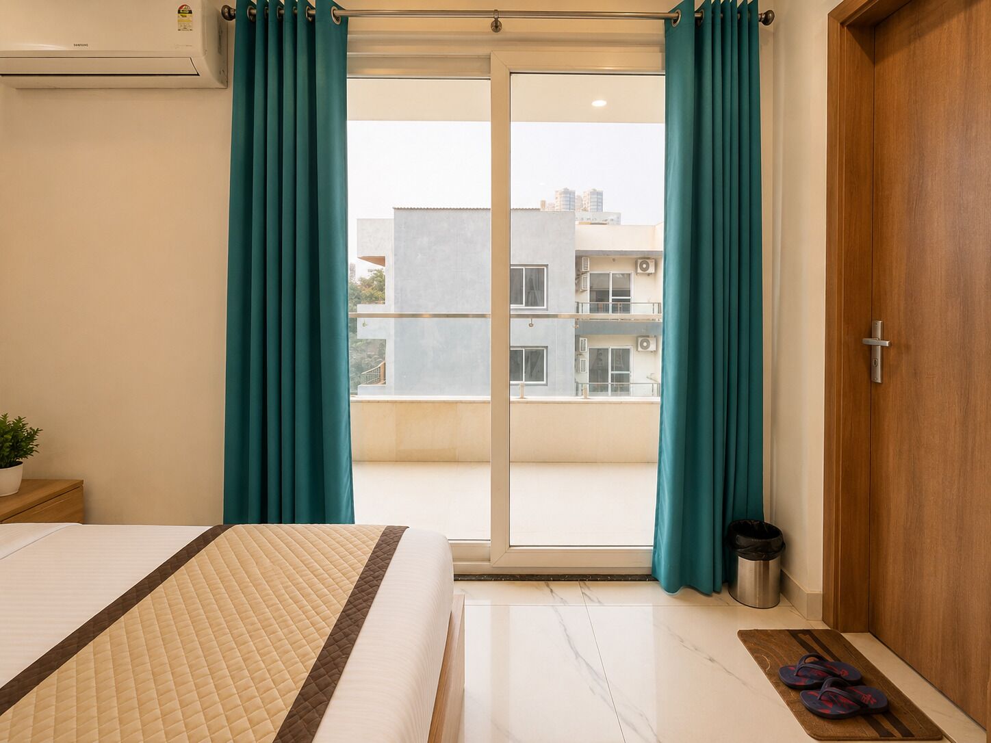 A hotel room with a bed, a sliding glass door to the outside, a small trash bin, and a wooden door.