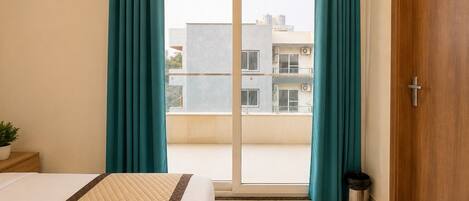 A hotel room with a bed, a sliding glass door to the outside, a small trash bin, and a wooden door.