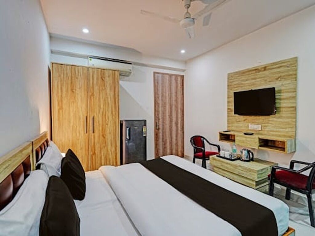 A hotel room with a bed, a desk, a chair, a television mounted on the wall, and a wardrobe.
