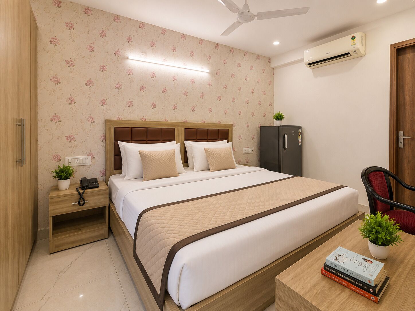 A hotel room with a bed, bedside table, nightstand, and a desk with a chair and a potted plant.