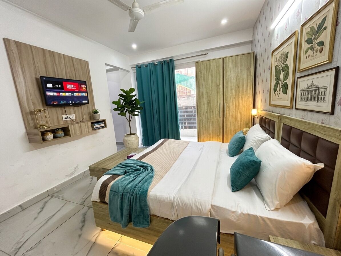 A hotel room with a bed, a television mounted on the wall, a plant, and a view of the outside.