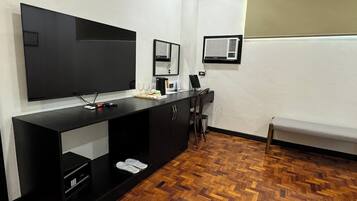 Quarto moderno com uma grande televisão de tela plana na parede, uma escrivaninha preta com um computador e um pequeno espaço de estar com um banco.