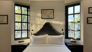 A neatly made bed in a room with large windows, a framed map on the wall, and a wooden floor.