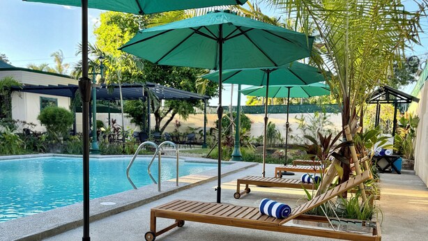 A poolside area with wooden lounge chairs, green umbrellas, and a clear view of the pool.