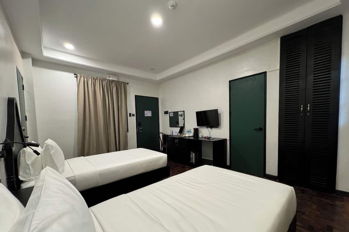 A hotel room with two single beds, a desk with a computer and a flat-screen TV, a wardrobe, and a mirror.