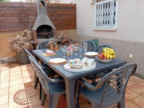 A dining table set outdoors with chairs, plates, glasses, and a bowl of fruit. - Casa LiaRAMBLA MALLOLS 9, CASA LIA (L'Escala)