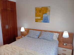A bedroom with a bed, two bedside lamps, a wooden wardrobe, and a painting on the wall. - Casa LiaRAMBLA MALLOLS 9, CASA LIA (L'Escala)