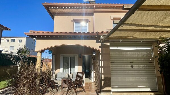 A two-story house with a covered patio, a garage, and a small garden area.