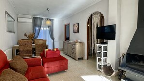 A living room with a red sofa, a television, a fireplace, wicker furniture, and a dining area with a table and chairs. - Casa LiaRAMBLA MALLOLS 9, CASA LIA (L'Escala)