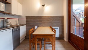 A compact kitchen with a wooden table and chairs, a dishwasher, and a built-in oven. - Apartment in Morillon with Pool & Mountain Views (Morillon)