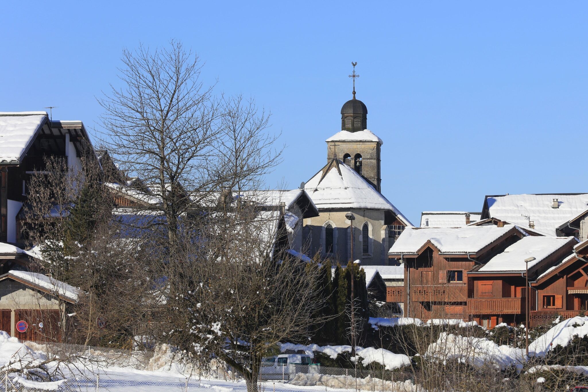Ein traditionelles Holzhaus mit verschneietem Dach, einem Glockenturm und wolkenlosem, blauem Himmel.
