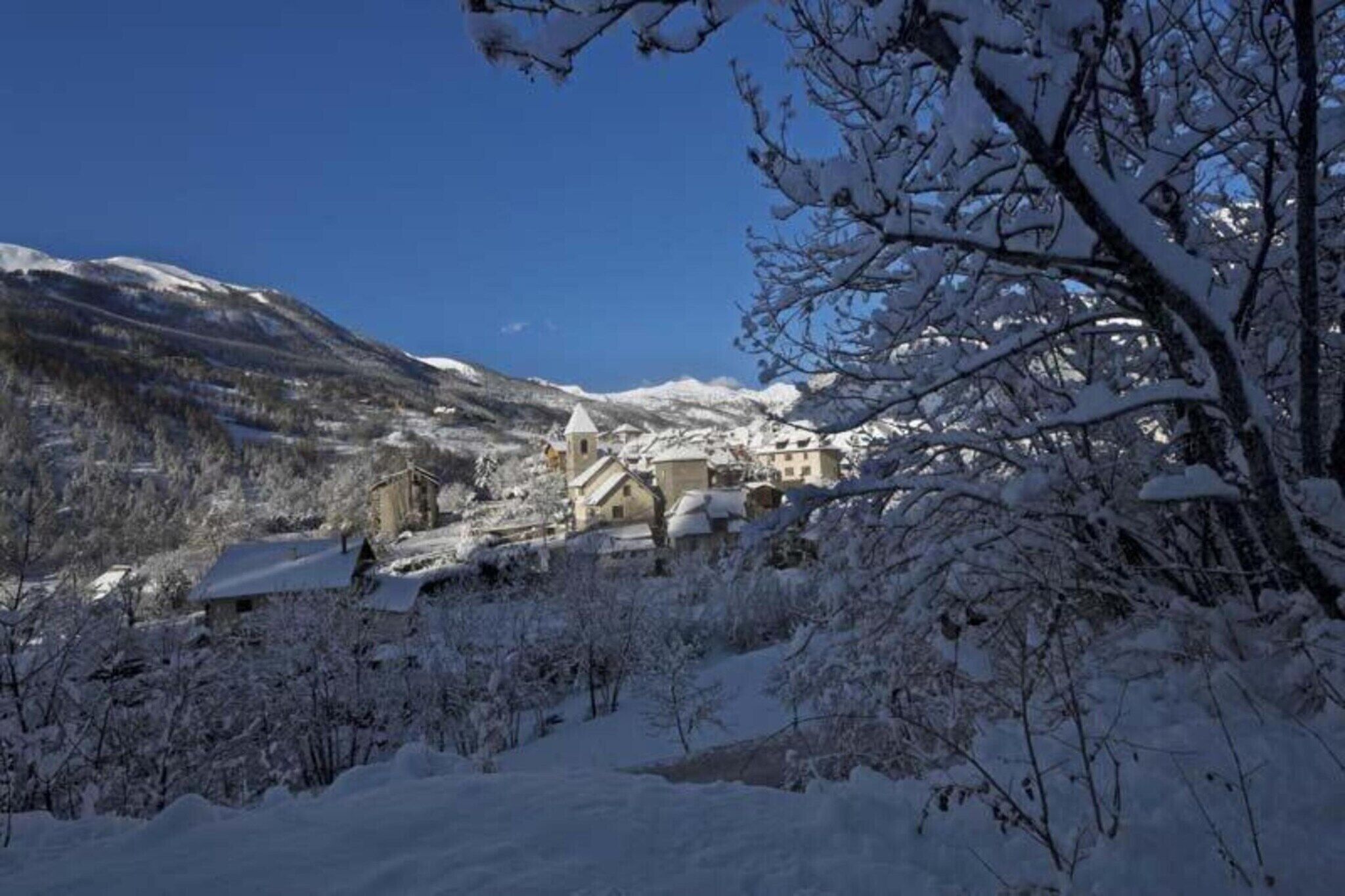 Un villaggio innevato con edifici tradizionali, una chiesa e montagne sullo sfondo.