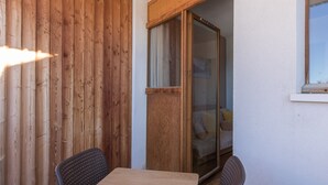 A room with a wooden wall, a sliding glass door leading to a bed, a small table, and two chairs. - Sunny Mountain Retreat (Orcières)
