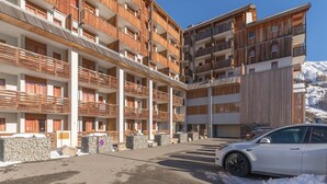 A multi-story hotel with balconies, stone walls, and a parking area with a white car. - Sunny Mountain Retreat (Orcières)