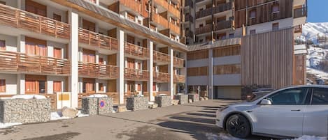 Un hôtel à plusieurs étages, doté de balcons, de murs en pierre et d’un parking où se trouve une voiture blanche.