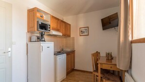 A compact kitchen with wooden cabinets, a microwave, a refrigerator, and a dishwasher. There's a small dining table with chairs and a TV mounted on the wall. - Sunny Mountain Retreat (Orcières)