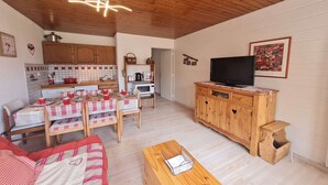 Ein gemütliches Wohnzimmer mit Holzbalkendecke, einem Essbereich mit rot-weißer Karotischdecke und einem Fernseher auf einer Holzkommode.