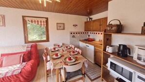 Eine gemütliche Küche mit Holzausbau, einem Esstisch, der mit rot-weißem Geschirr gedeckt ist, einem roten Sofa und einem Fenster mit Blick auf Grünflächen.