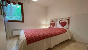 Ein Schlafzimmer mit Bett, einem Fenster mit Vorhängen, einer Wand mit herzförmigen Verzierungen und einem Nachttisch mit Lampe.