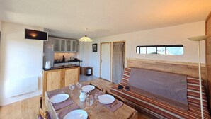 Ein gemütliches Zimmer mit einem Holzesstisch, gedeckt für vier Personen, einer Couch mit Kissen, einem an der Wand befestigten Fernseher und einem Fenster mit Außenblick.