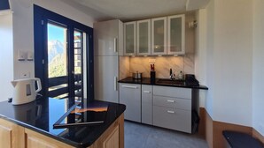Eine moderne Küche mit schwarzem Arbeitsplatz, weißen Schränken und Bergblick durch eine Tür.