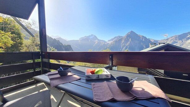 Ein Tisch mit Obstkorb, Schüsseln und einer hölzernen Bank mit Blick auf eine Berglandschaft.