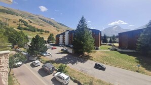 A parking lot with several cars, a building with multiple floors, and a mountainous backdrop.